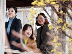 산수유 꽃망울 뒤로 정자에 올라가있는 아름다운 여성들이 웃으며 사진을 찍고 있는 모습이다.
