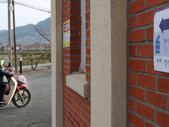 병영면 실내 게이트볼장에서 투표를 하고있다는 알림판이 건물벽에 붙어있고 그 옆으로 오토바이를 탄 두명의 사람이 투표소 방향쪽으로 가고 있는 모습이다. 