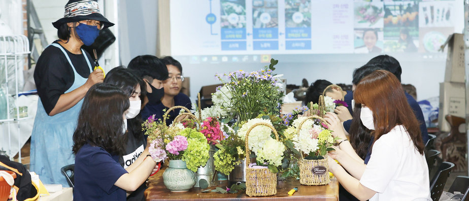 농장주가 가위를 들고 설명해주며 학생들이 모여앉아 꽃바구니를 만들고 있는 모습
